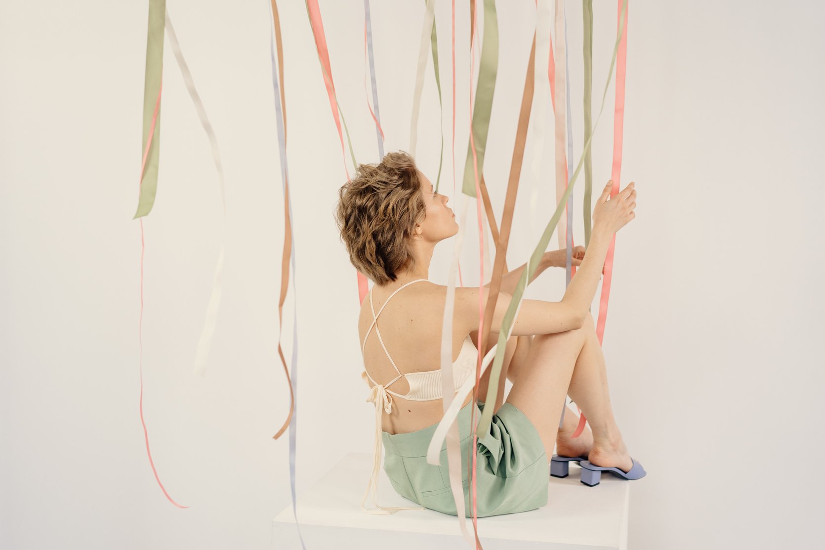 A Woman in White Bralette Sitting on the Floor while Touching Ribbons